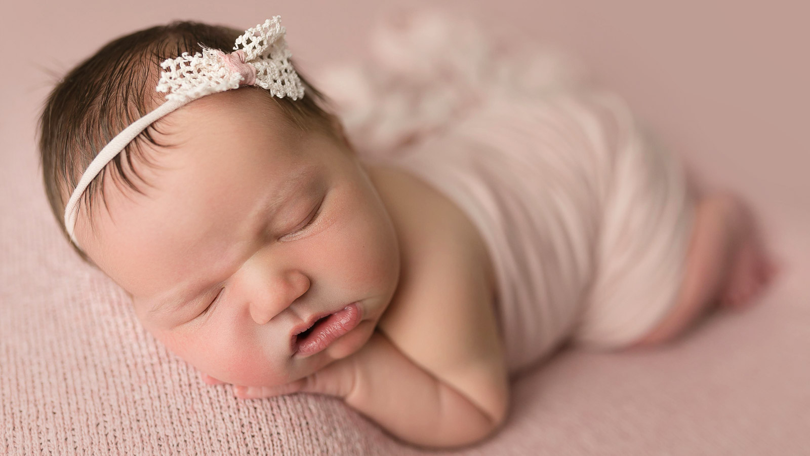 newborn studio photo of a baby girl in a pink wrap and matching bow in the des moines iowa area at my home photographer studio