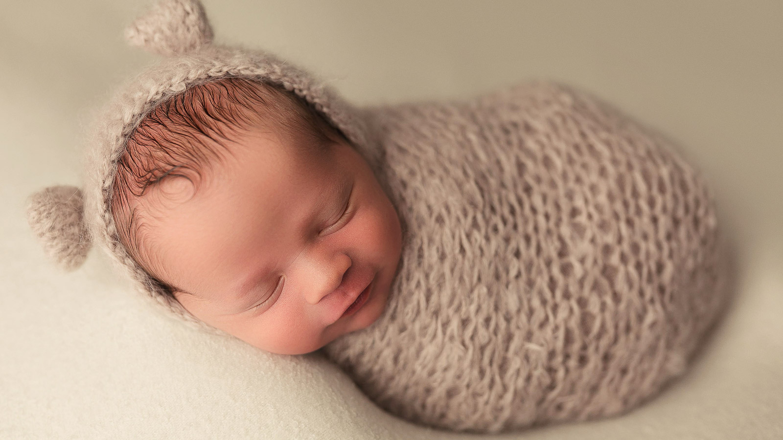 newborn studio portrait of a baby boy in a knitted teddy bear wrap and bonnet in ankeny iowa at my home photographer studio