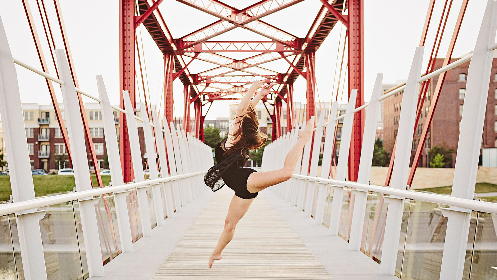 photograph of a senior girl wearing a black dance costume and dancing on a red bridge in the east village in des moines iowa