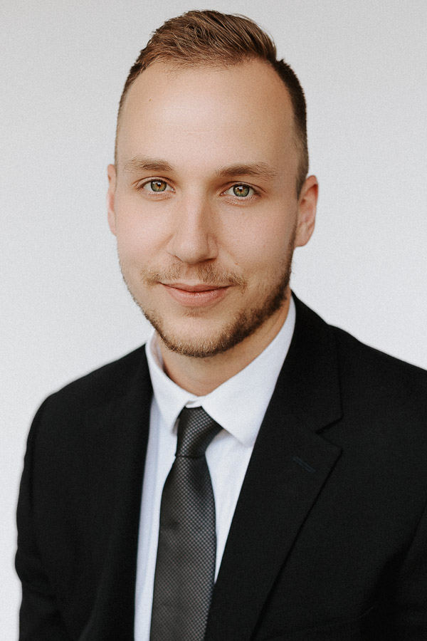 headshot of a man in a black suit with grey tie who works for health management associates. photo was taken on a white backdrop using only natural light.
